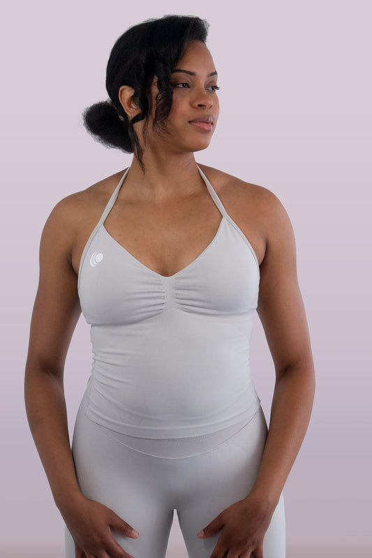 Woman wearing a light gray sports bra and leggings on a plain background